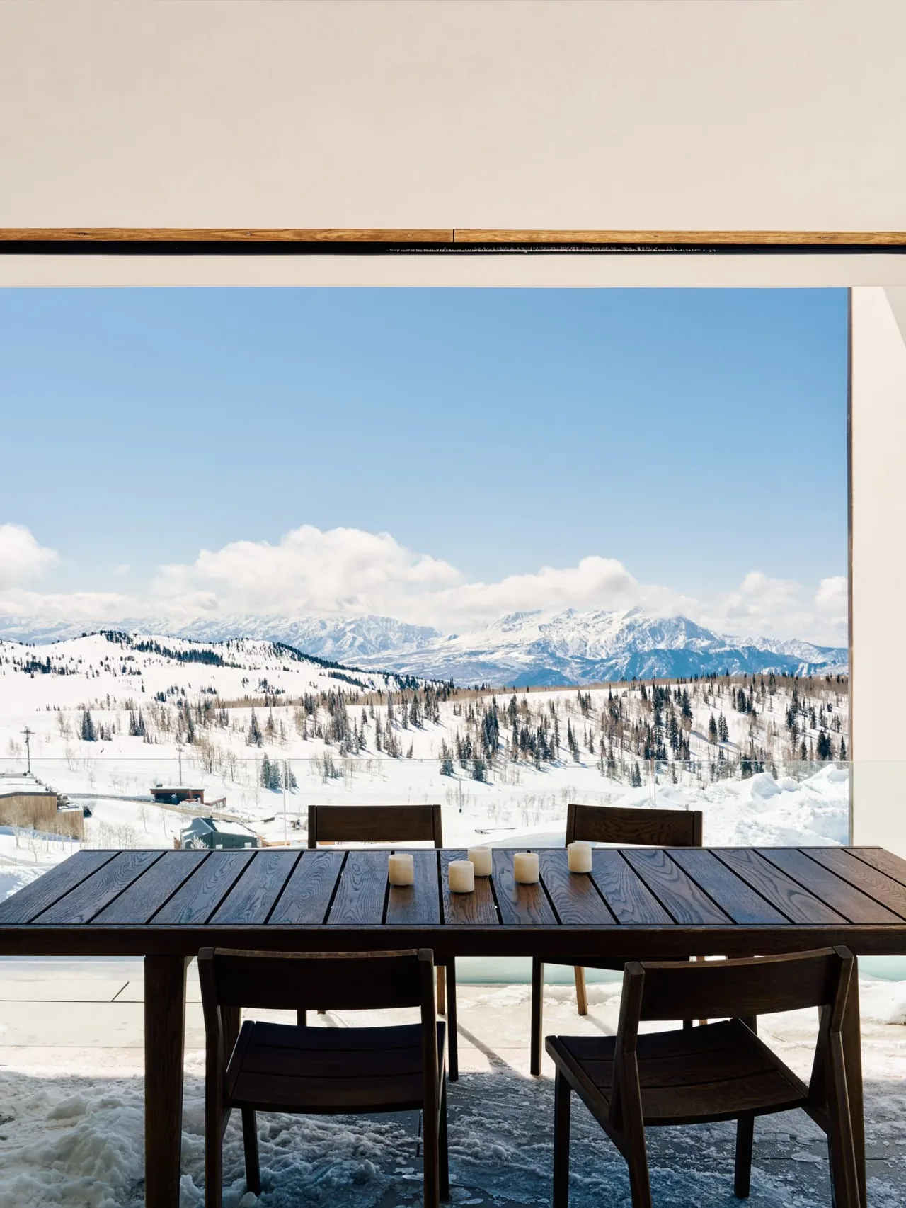 The Overlook Cabin features an outdoor dining area with a wooden table and chairs, overlooking snow-covered mountains.