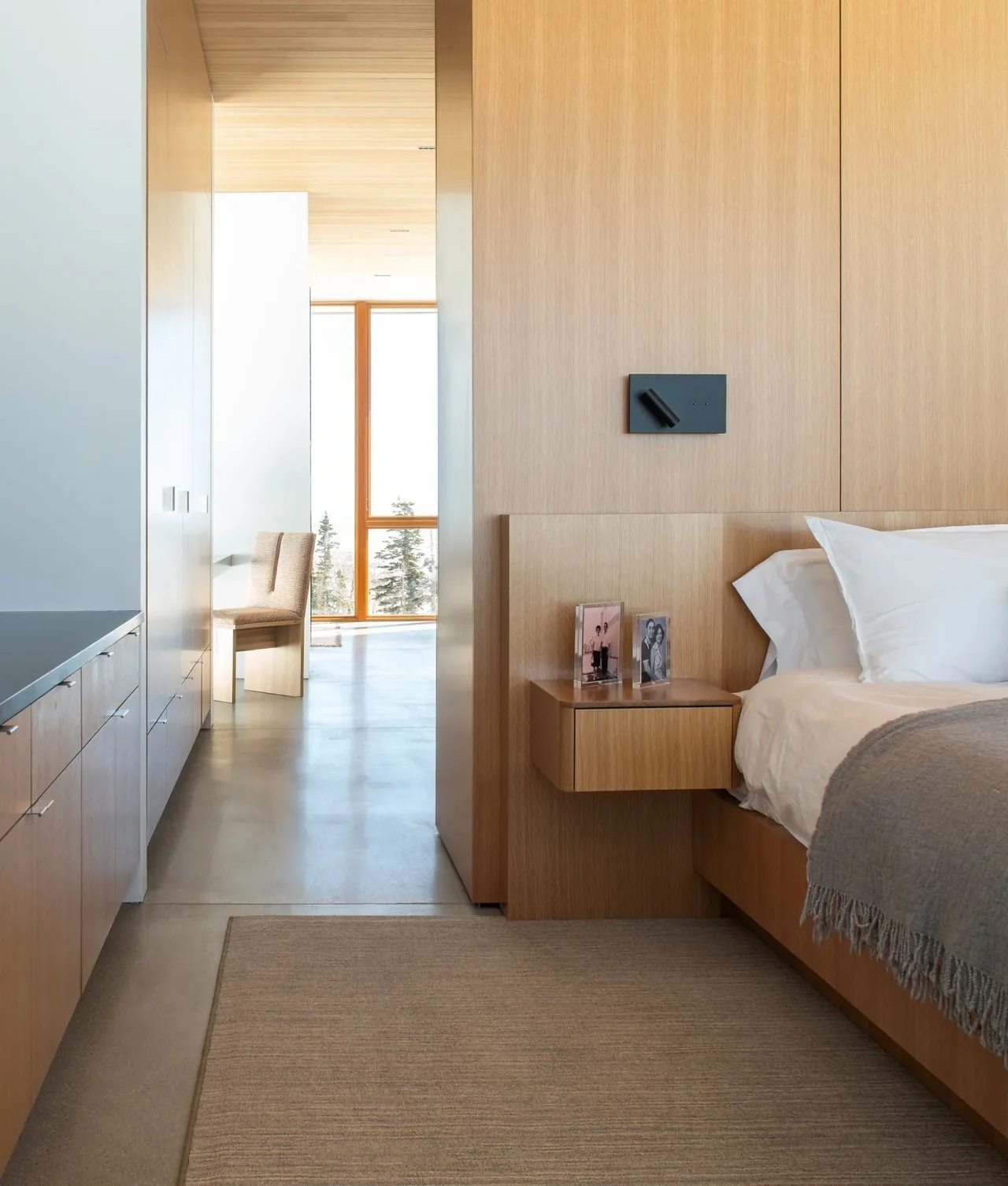 Bedroom corner features light wood paneling, a floating nightstand, and white bedding with a gray throw.