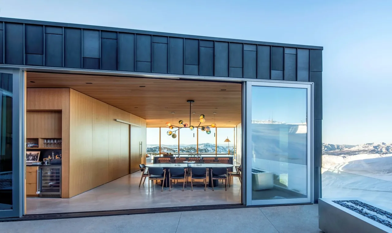 Dining room with wood paneling open to outdoor space and snowy mountain views at Kirigami project.