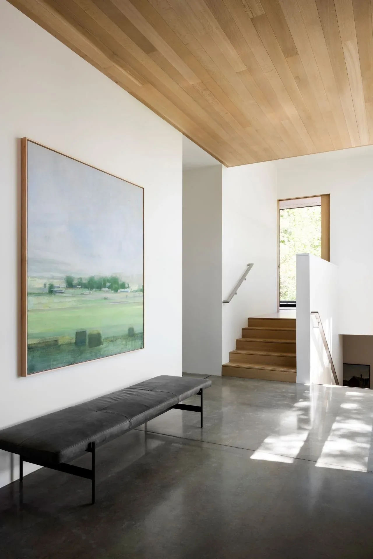 Entry hallway in Emigration Creek Residence features a wood ceiling, polished concrete floor, bench seating, and a landscape painting.