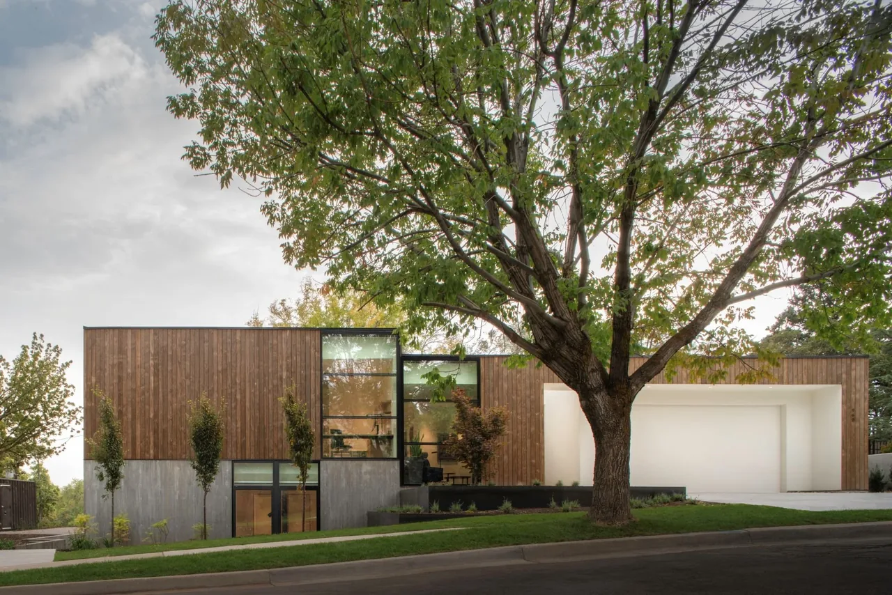 Emigration Creek Residence features wood siding and large vertical glass windows with a white framed garage entrance.