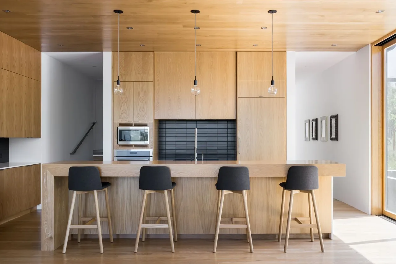 Kitchen with wood-paneled ceiling and cabinetry, black tile backsplash, island seating, and pendant lights.