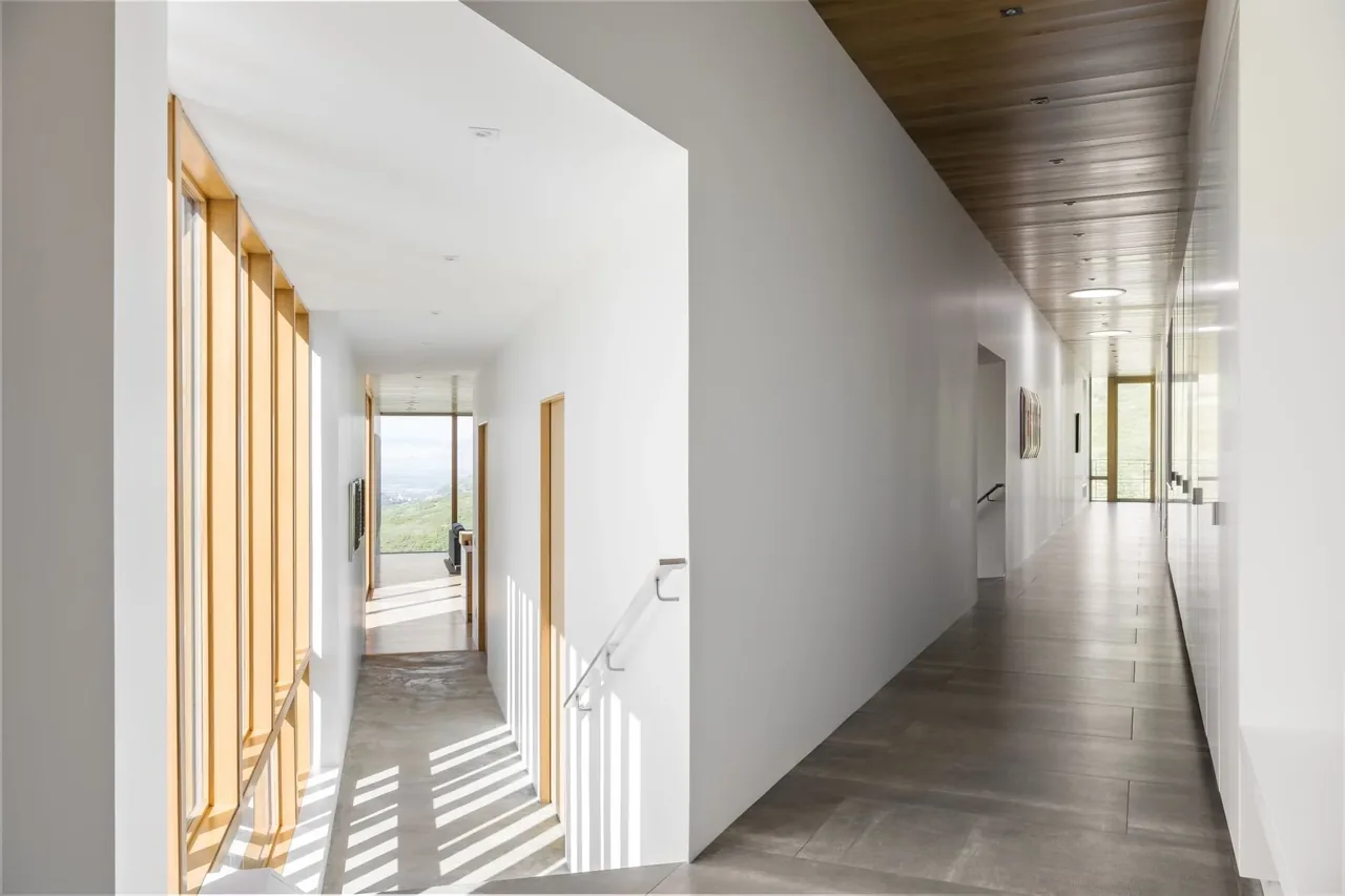 The Wabi-Sabi project features a bright, minimal hallway with wood ceiling panels and panoramic windows showing hilltop views.