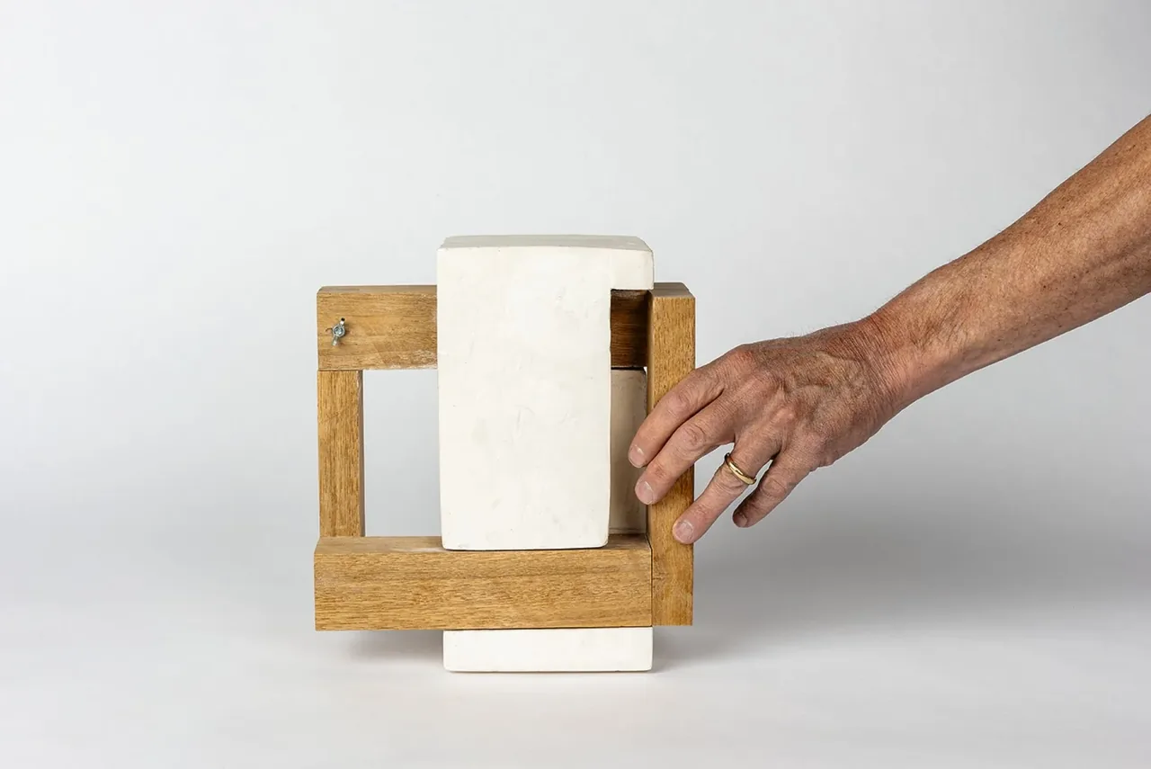Small architectural model combining wooden frame elements with white rectangular blocks.