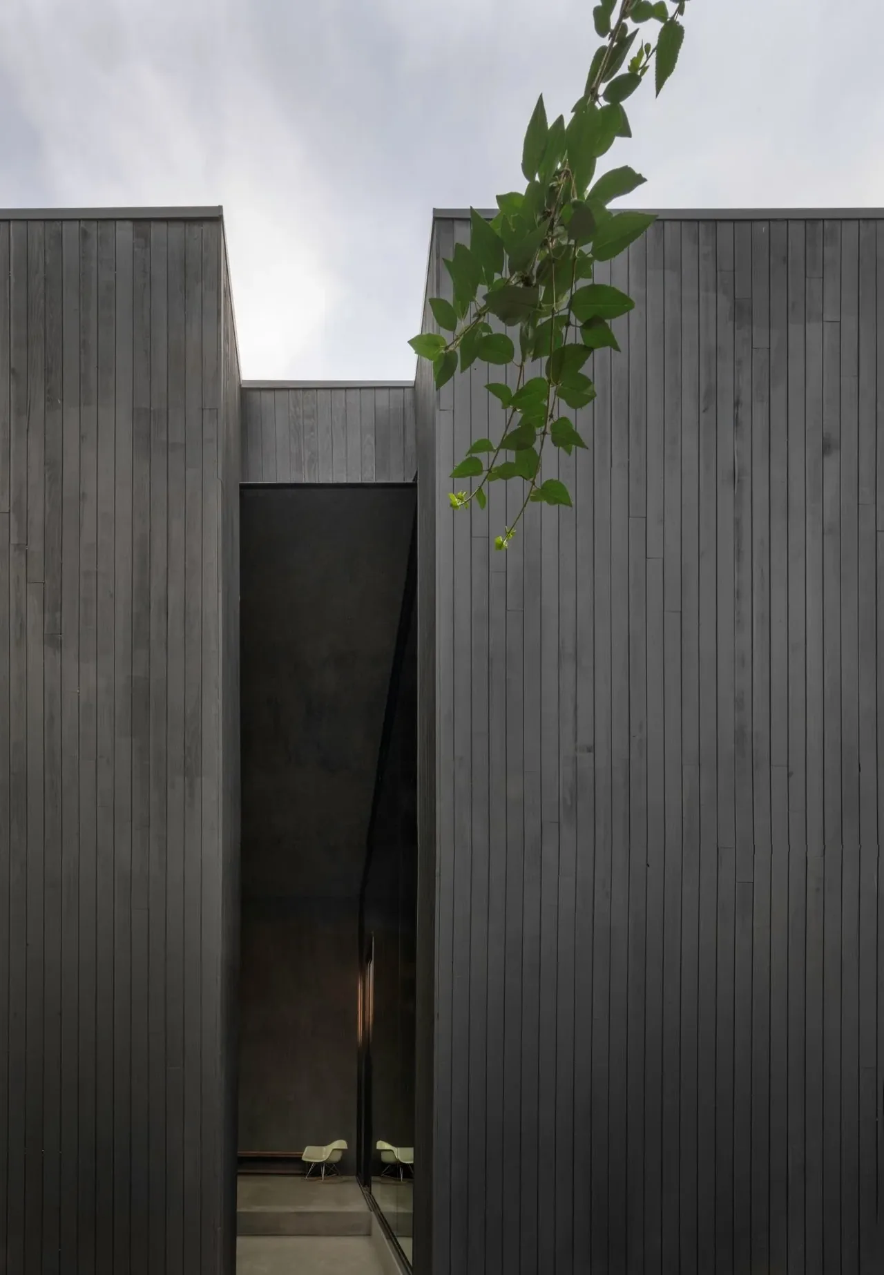 Exterior with vertical black wood siding and a narrow recessed glass opening showing part of the interior seating.