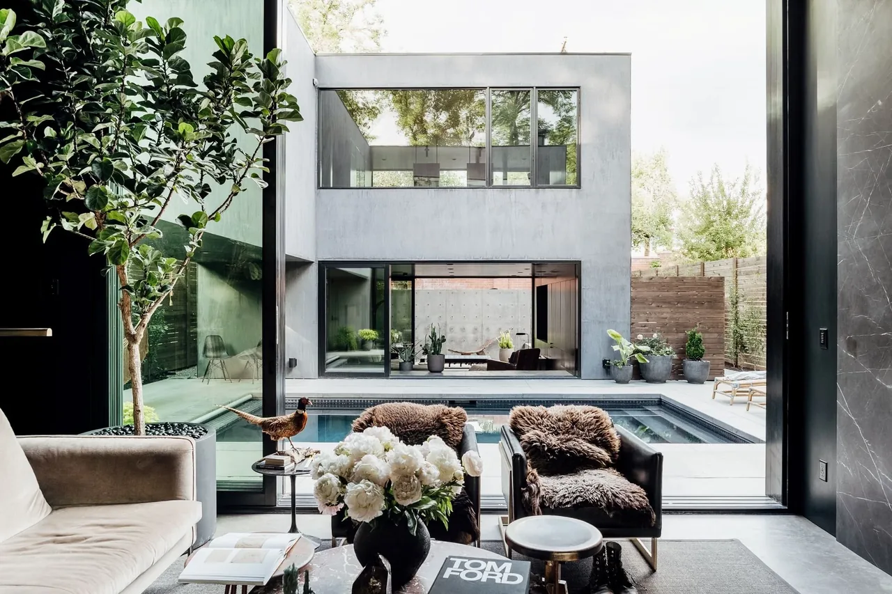 Indoor living area looking out to concrete outdoor pool and modern two-story building with large windows
