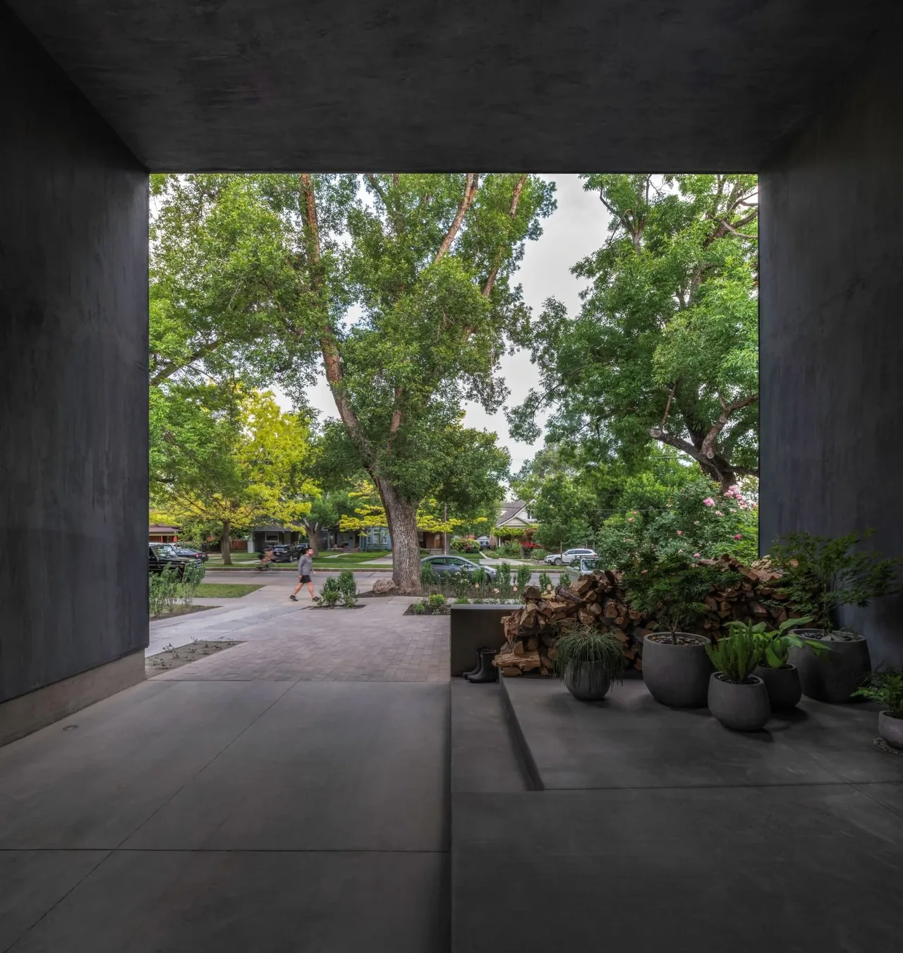 Concrete outdoor living area opening to a neighborhood street with mature trees and landscaping.