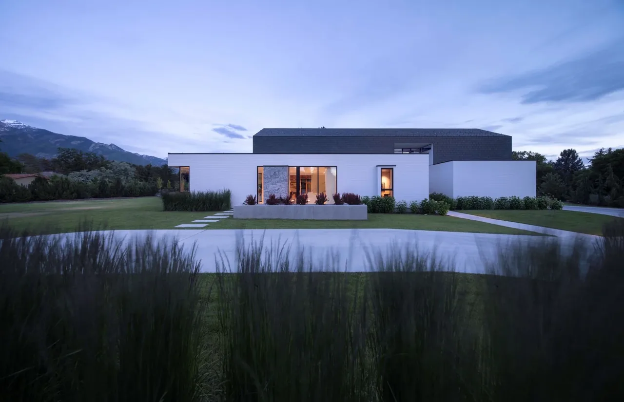 Exterior rear view of a modern farmhouse with flat roof and landscaping, featuring a concrete planter and large windows.