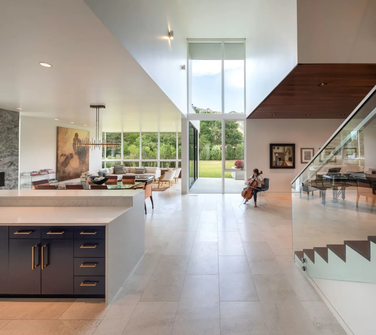 Modern open living area featuring floor-to-ceiling glazing, glass stair railing, and navy blue kitchen cabinets.
