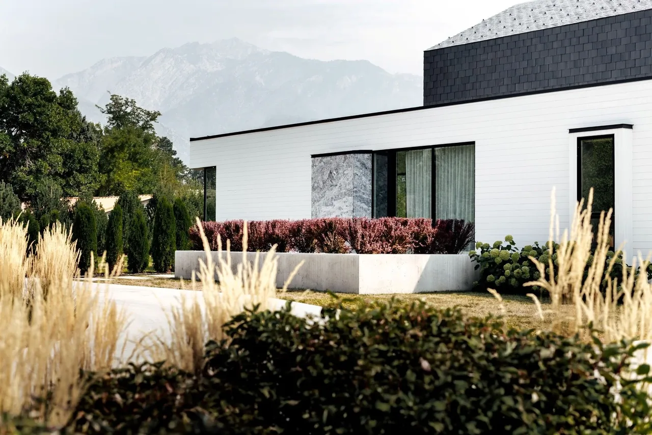 Modern farmhouse exterior featuring white wood siding, black window frames, and concrete planter with bushes.