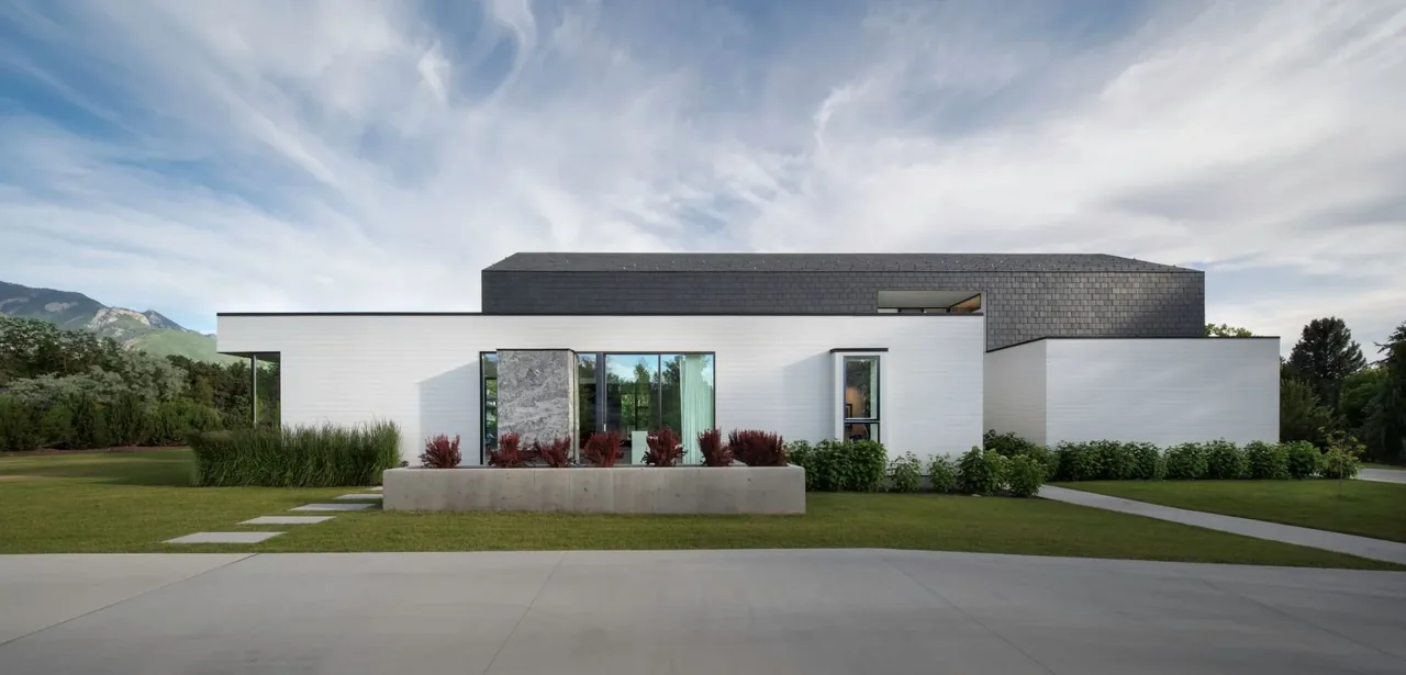 Side view of a modern farmhouse with white walls and a dark gable roof under a cloudy sky.