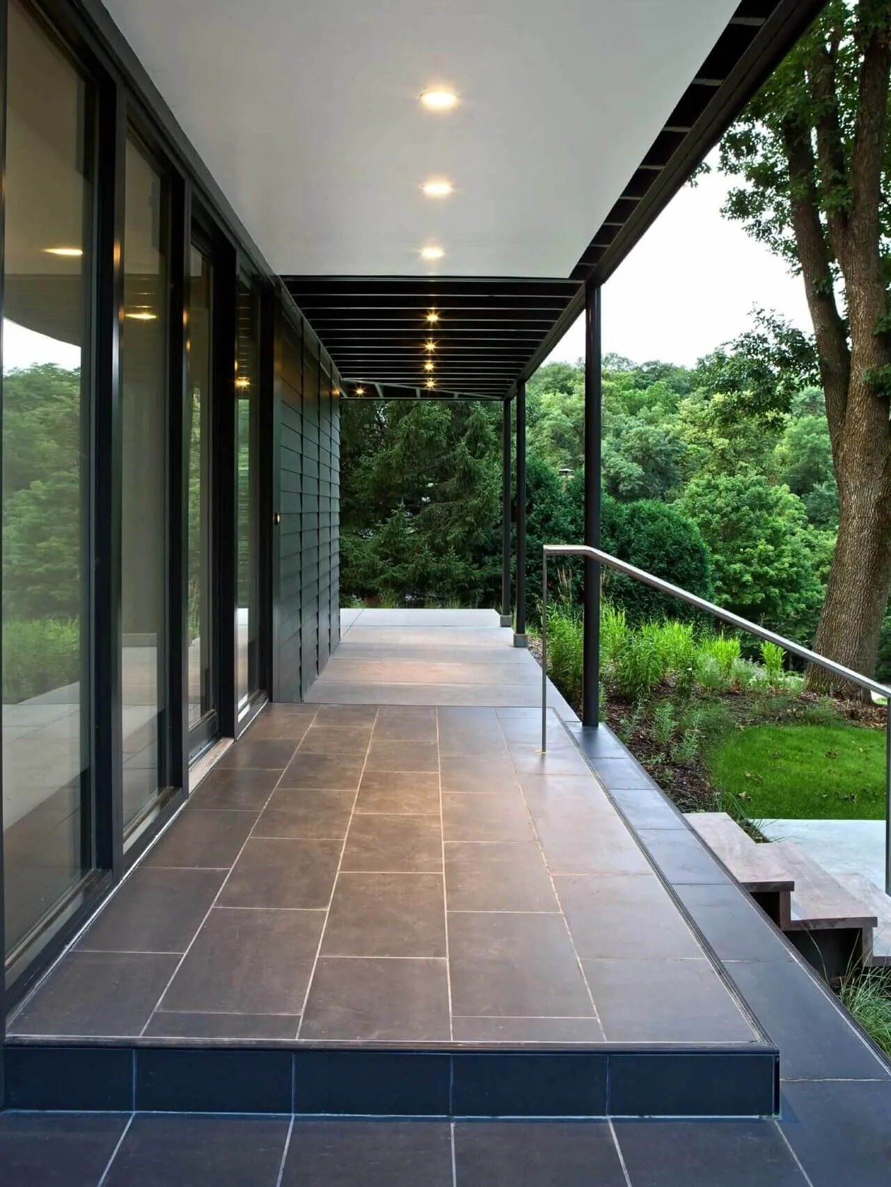 Porch of '322 Reinvented' features gray tile flooring, black metal handrail, and recessed patio lighting by Substance Architecture.