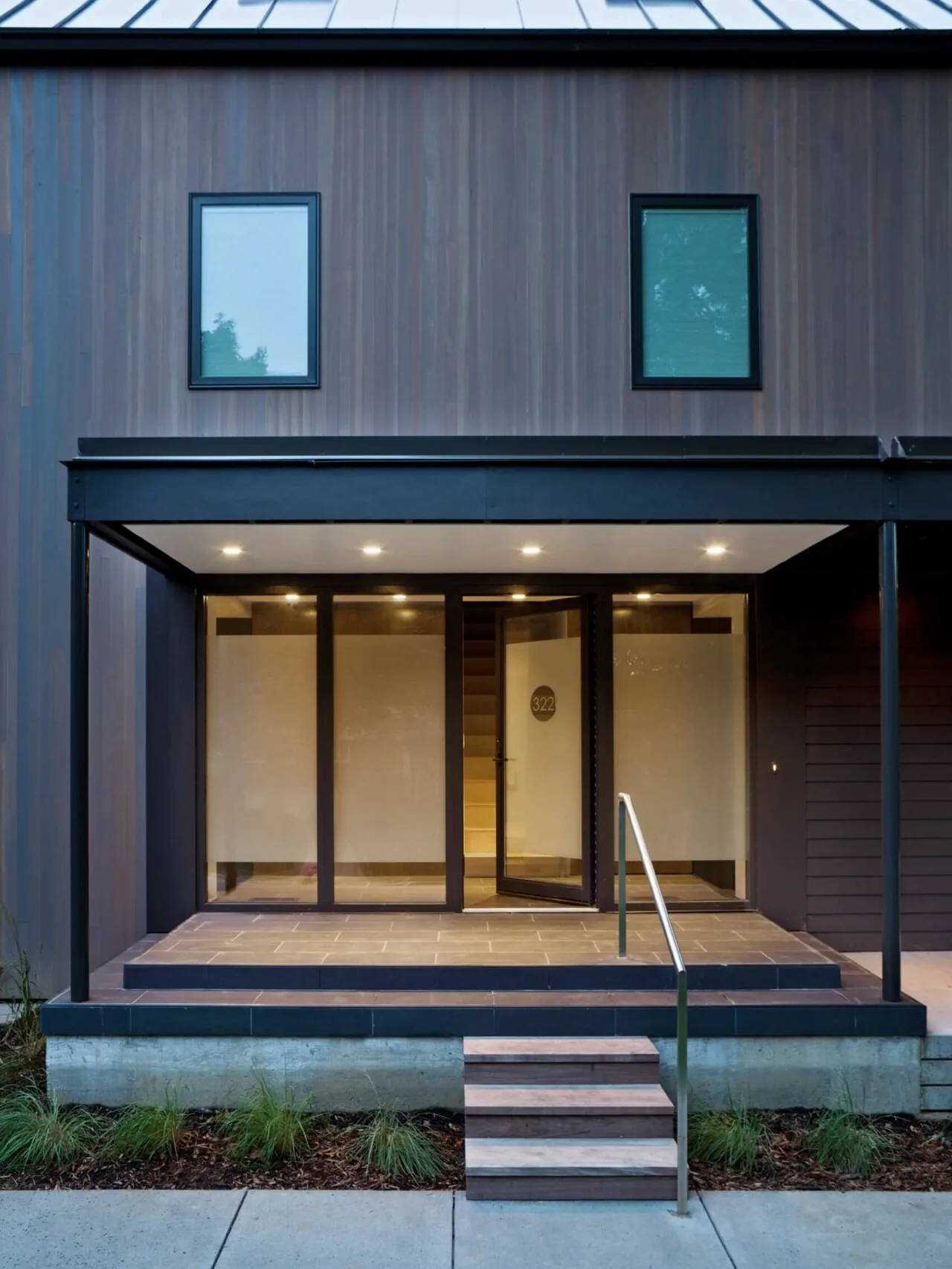 The 322 Reinvented project features a modern front exterior with vertical wood siding and a covered porch illuminated by recessed lighting.