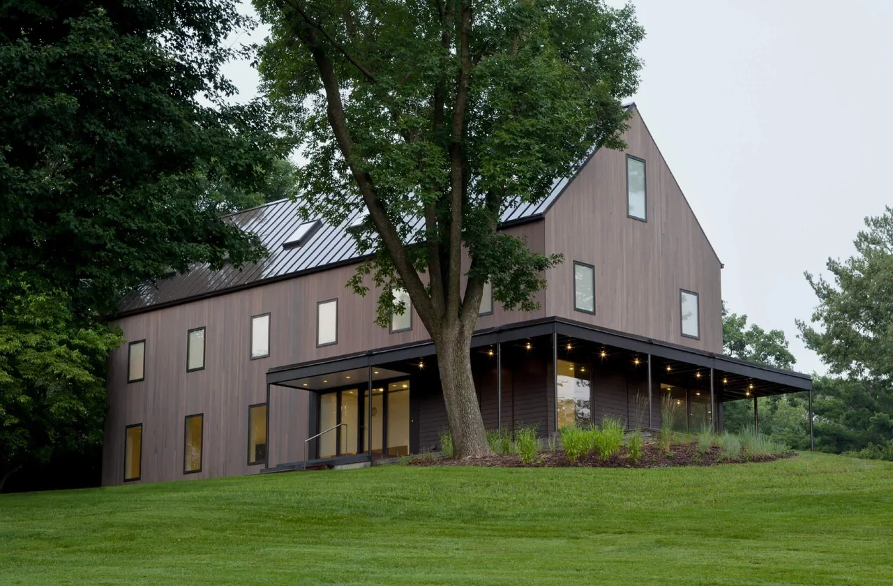 322 Reinvented features vertical wood siding, a standing seam metal roof, and a recessed patio with lighting at night.