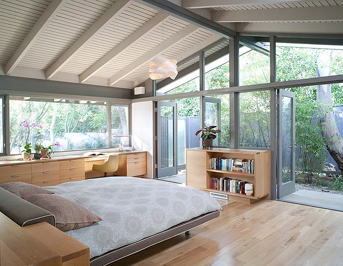Canon Residence bedroom featuring an angled ceiling, built-in desk, bookshelf, and floor-to-ceiling windows that open to the outside.