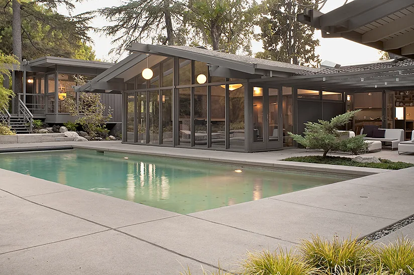 The Canon Residence features a raised concrete deck surrounding a rectangular pool with large floor-to-ceiling windows and a metal pergola.