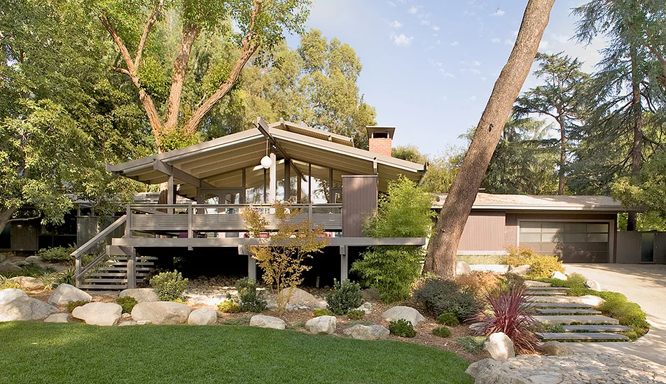 Midcentury modern Canon Residence features a raised deck with metal pergola and large windows under a gable roof.