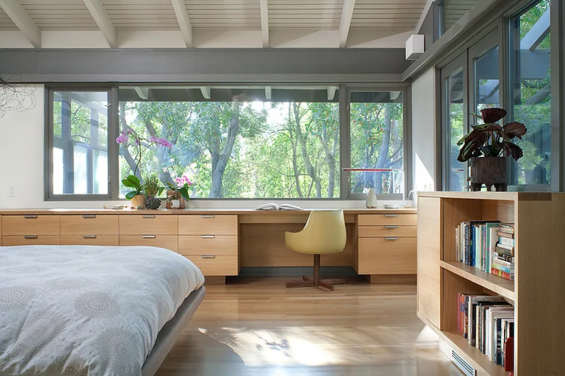 The Canon Residence bedroom includes large windows with gray frames, a built-in wooden desk, and wood flooring.