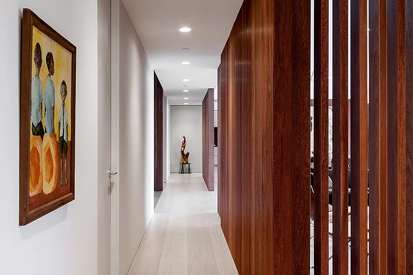 Hallway in the Arby Residence featuring light wood flooring and a slatted wood wall with artwork and a sculpture.