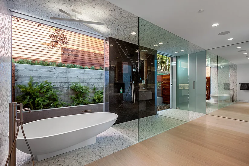 The Arby Residence bathroom features a freestanding tub and a glass-enclosed shower with garden views.