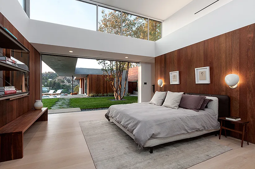 Bedroom in Arby Residence features a wood accent wall, clerestory windows, and an open wall that connects to the backyard.