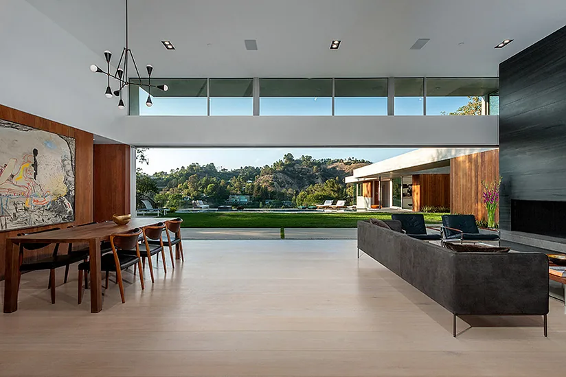 Open living and dining area with floor-to-ceiling glazing overlooking the lawn and hillside at Arby Residence.