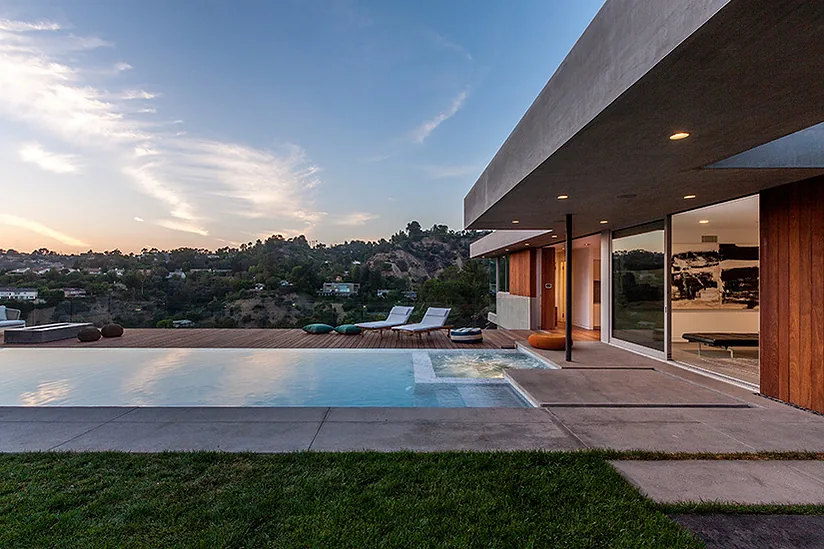 The Arby Residence features a rectangular illuminated pool with an attached spa and wood decking extending from the modern two-story house.