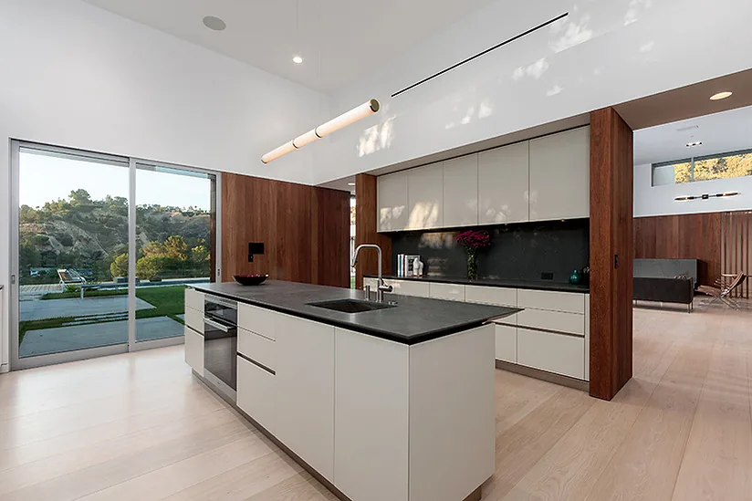 The Arby Residence kitchen features a large island with a dark countertop, white cabinets, and sliding glass doors leading to the backyard pool area.