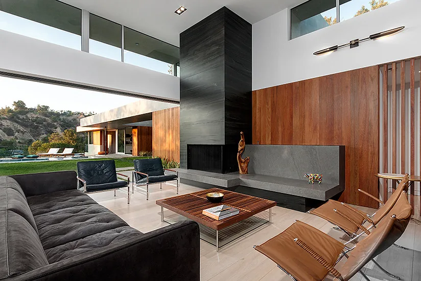 Living room in the Arby Residence showing floor-to-ceiling glazing, a black fireplace, and wood-paneled walls by Space International Inc.
