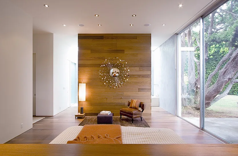 Bonsall Residence bedroom features a large floor-to-ceiling glass window with views of a tree and landscaped outdoor space.