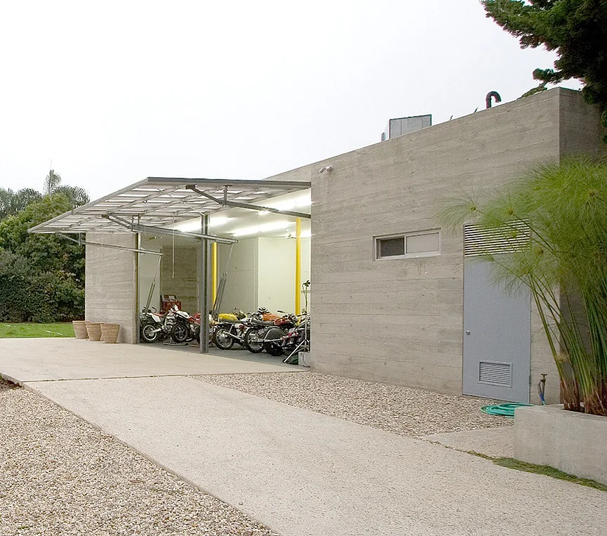 Garage exterior of the Bonsall Residence with a board-formed concrete facade and narrow horizontal window above a metal door.