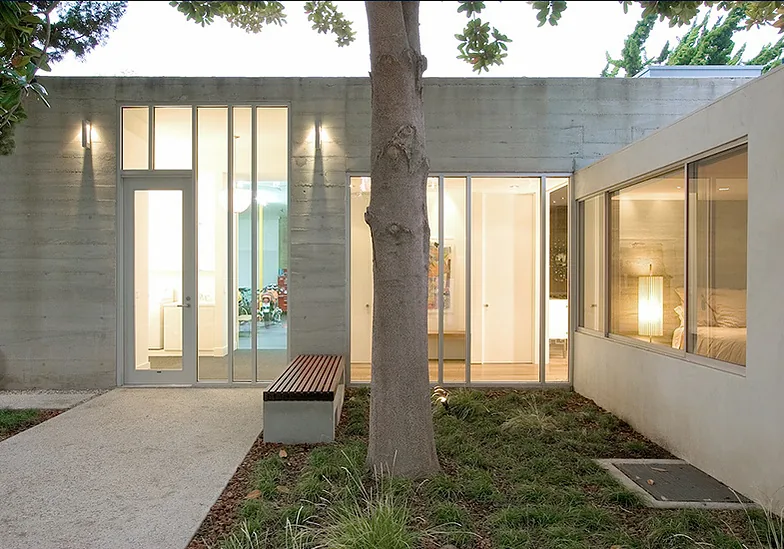 The Bonsall Residence features a concrete facade with narrow vertical windows and an exterior bench under tree canopy.