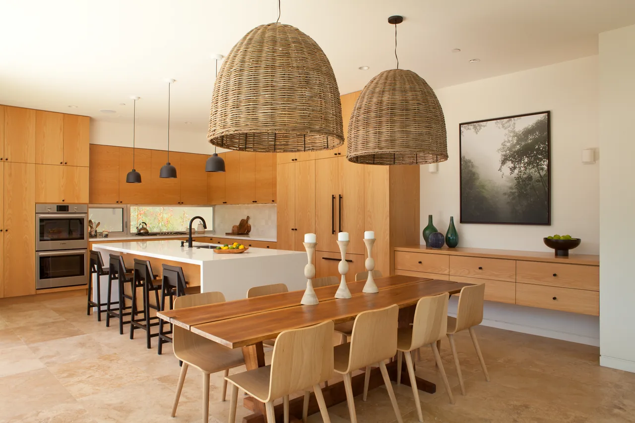 The Clark Street Private Residences kitchen features light wood cabinets, a white island, dining table, and woven pendant lighting.