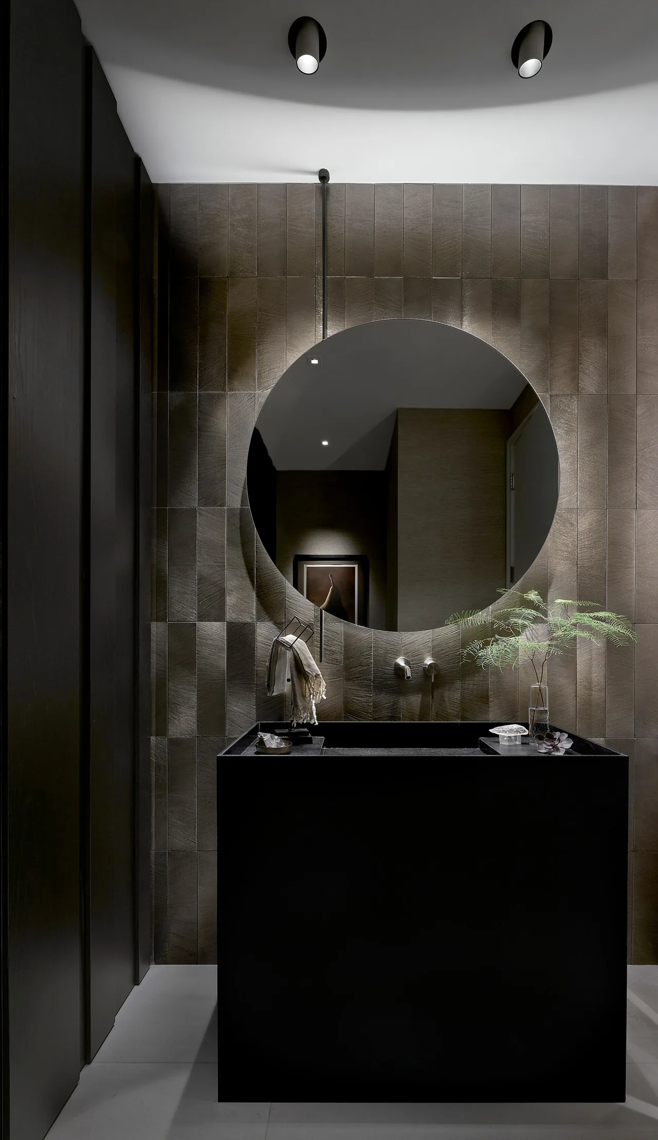Modern bathroom with a black rectangular sink vanity and a large circular mirror on a textured tile wall.