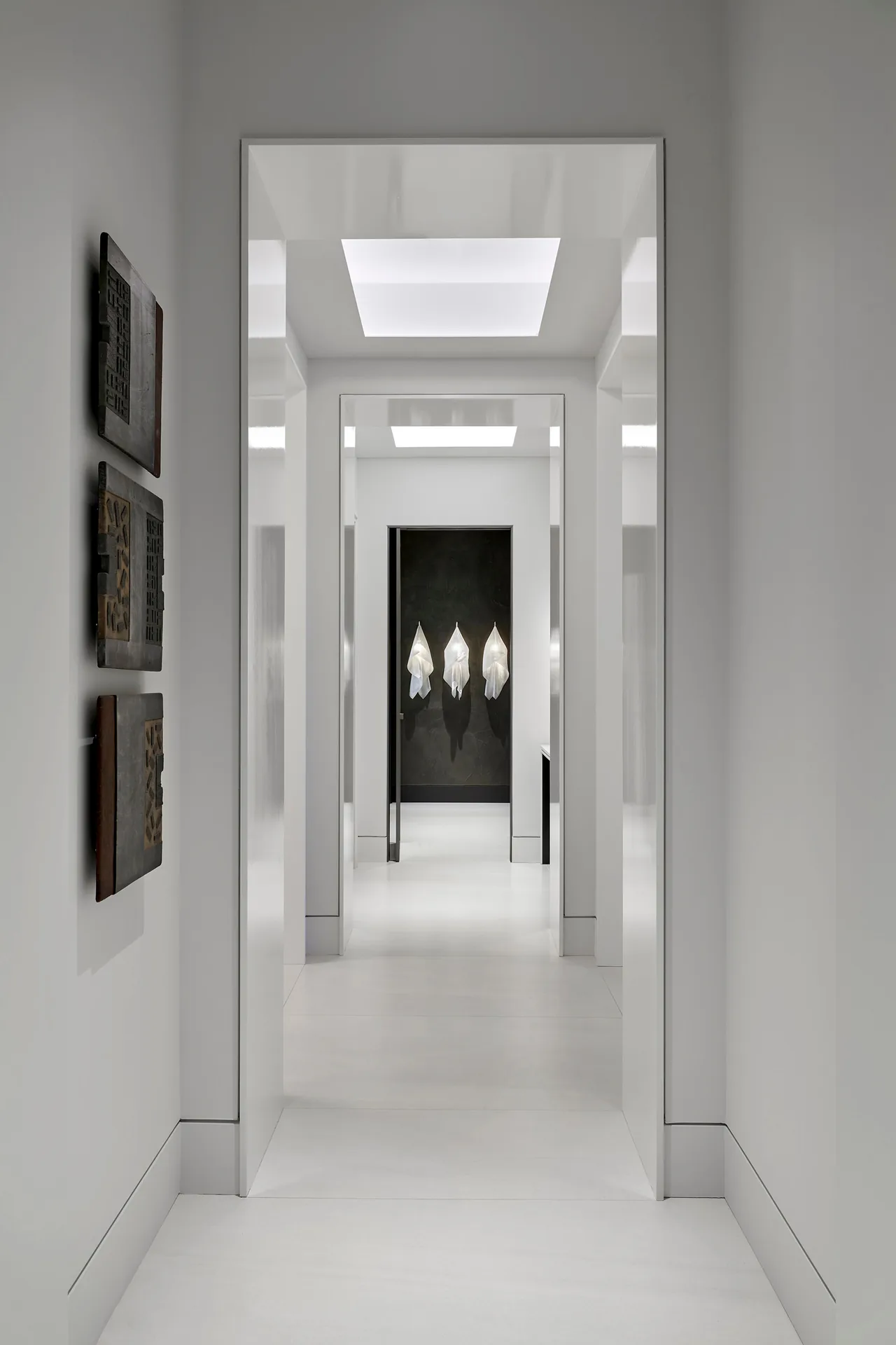 A minimalist white hallway with recessed ceiling lights and art installations at the far end.