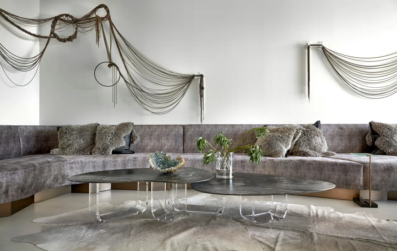 Inside the Art House project, a living room features a curved gray sectional sofa and sculptural wall-mounted chains.