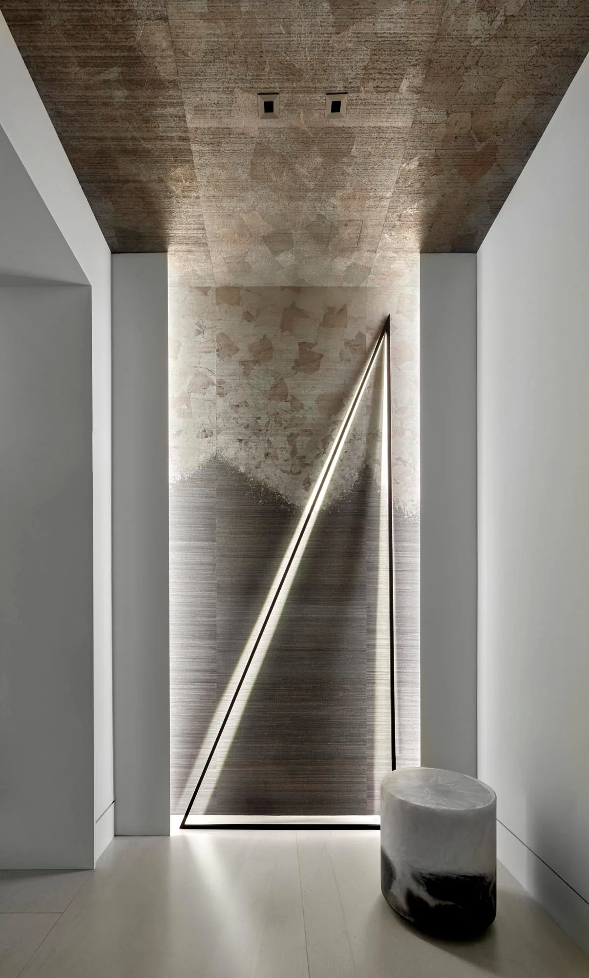 Art House entry features a textured wall with an illuminated triangular frame and sculptural stool.