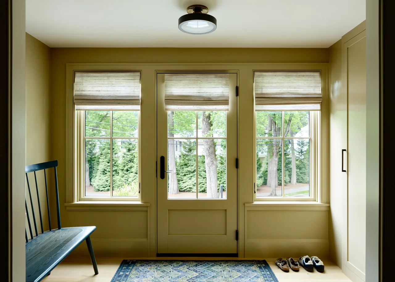 Bright entry space with three-paneled door and adjacent windows featuring beige walls, a dark bench, and a patterned rug.