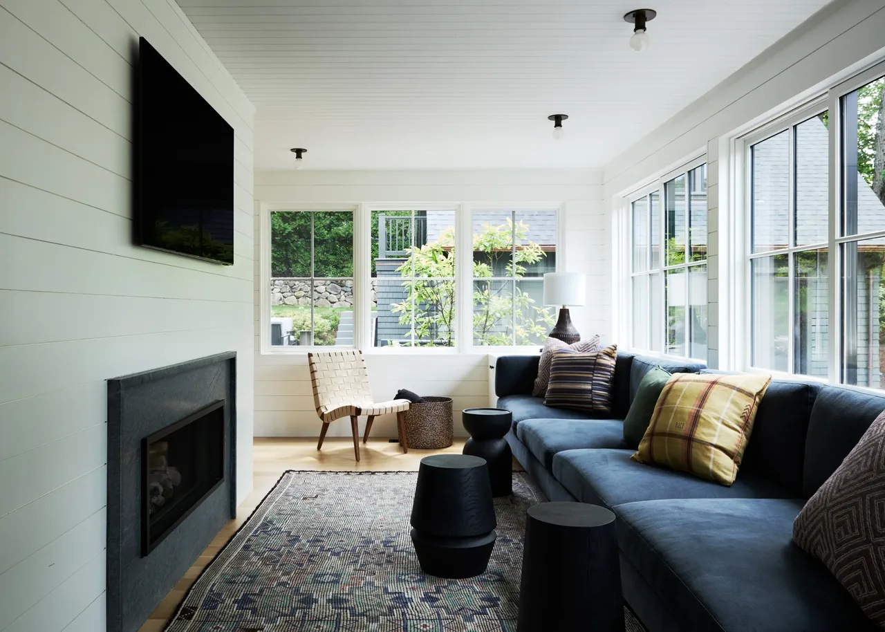 Living room in Valentine House features large windows, a sectional sofa with patterned cushions, and a fireplace under a mounted TV.