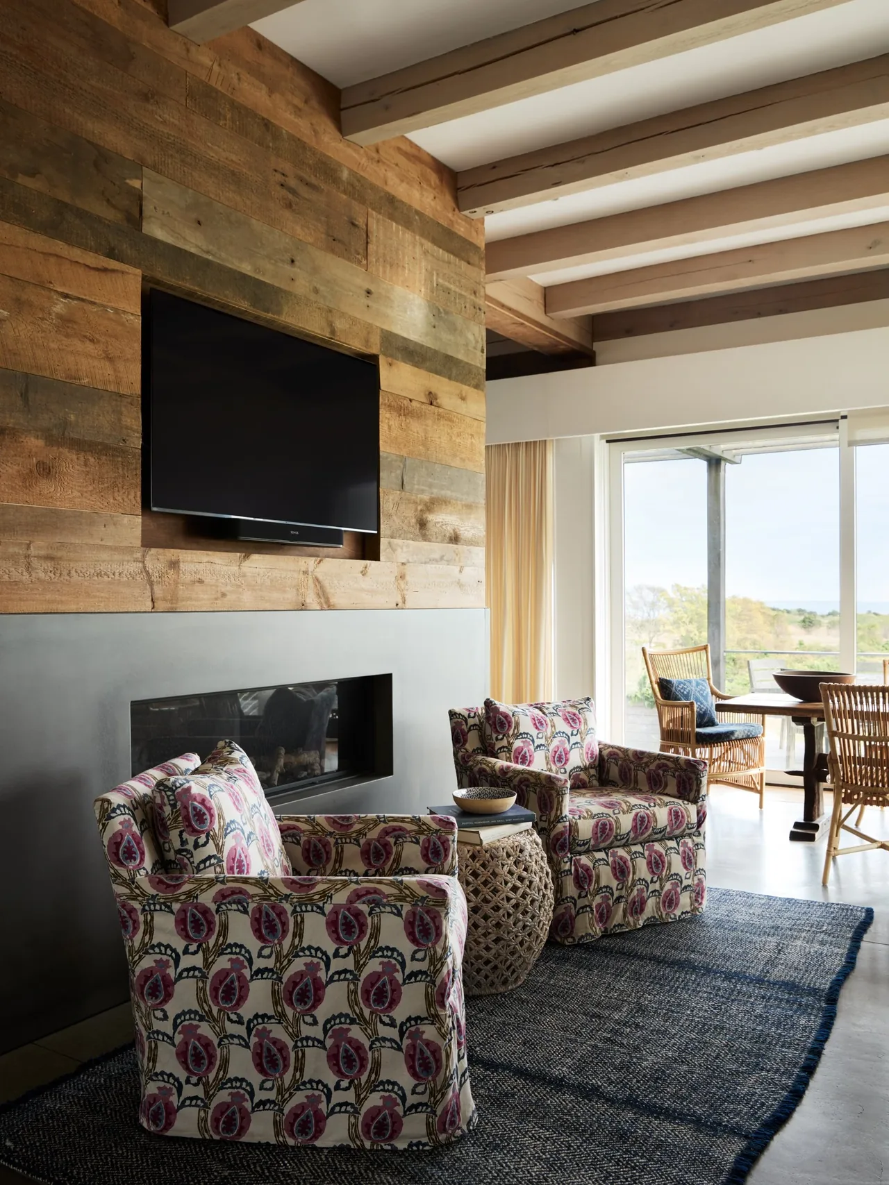 Living room features patterned armchairs and a TV mounted on a reclaimed wood-paneled wall with exposed ceiling beams.