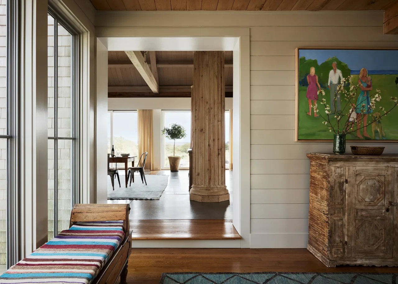 The hallway features a rustic wooden pillar and cabinet, with a bench by the window and a dining room visible beyond.