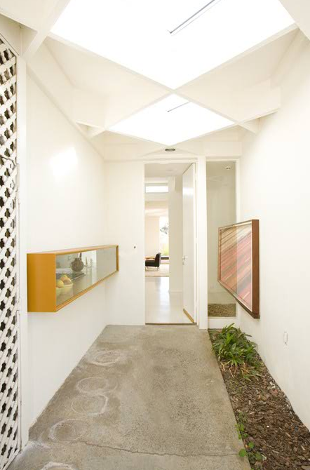 The narrow hallway features white walls, a concrete floor, skylights, and an indoor garden bed, part of the Casiano Residence by Assembledge Architects.