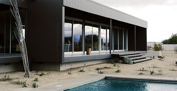 Rear exterior of Desert House with floor-to-ceiling glazing, flat roof, and a rectangular pool amidst desert landscaping.