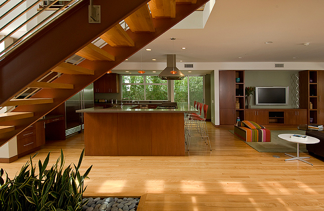 Open kitchen and living area with wood flooring, floating wood stairs, and built-in entertainment cabinetry at Herron Residence.