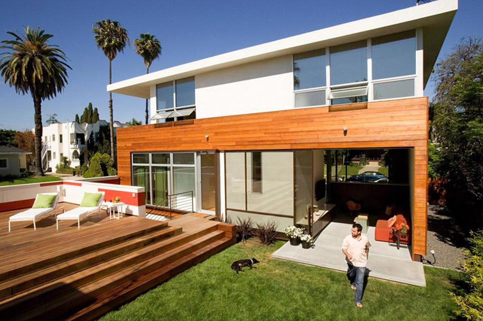 Ridgewood Residence features horizontal wood siding, floor-to-ceiling glazing, a flat roof, and a covered patio with outdoor seating.
