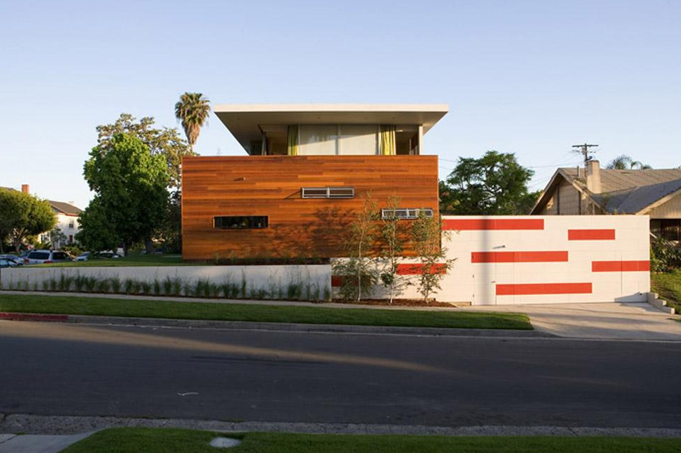 Ridgewood Residence features wood siding on the second story and a flat roof above a white and red garage wall.