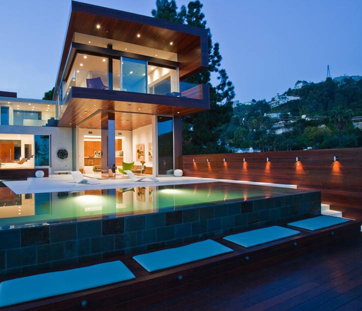 Sunset Plaza Residence shows a modern style with a cantilevered wood-paneled upper floor, pool, and recessed lighting on the patio.