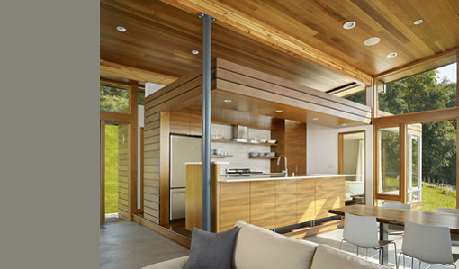 Vashon Cabin kitchen features wood paneling, minimalist cabinetry, open shelving, and expansive windows for natural light.