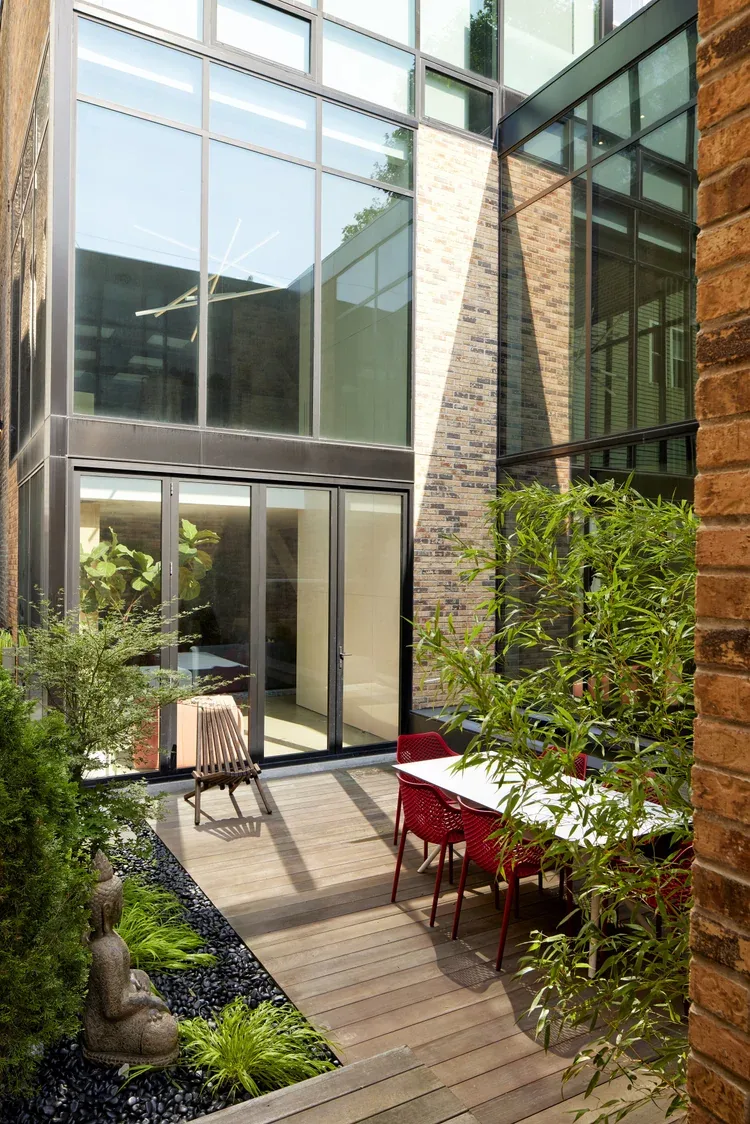 The outdoor patio features wood decking, red dining chairs, and floor-to-ceiling windows connecting to the interior.