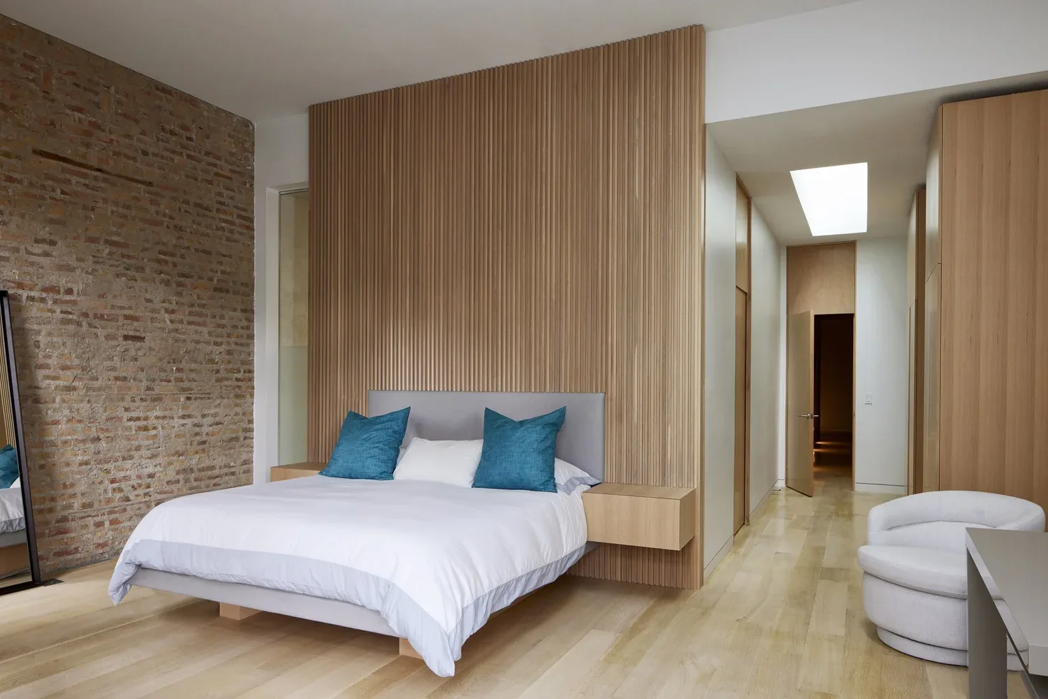 Bedroom features vertical wood slat accent wall, exposed brick, and skylight in hallway.